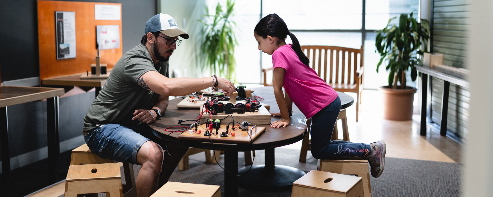 Decorative photo of a child and an adult at a table both interacting with a science exhibit.