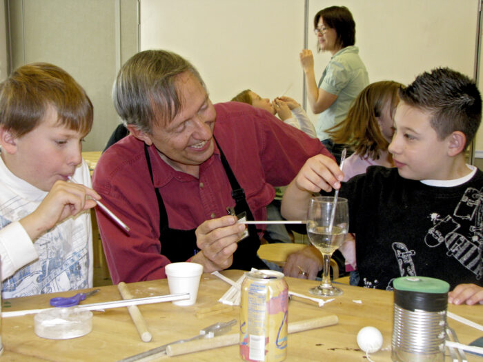 Volunteer works with students using straws in a science experiment