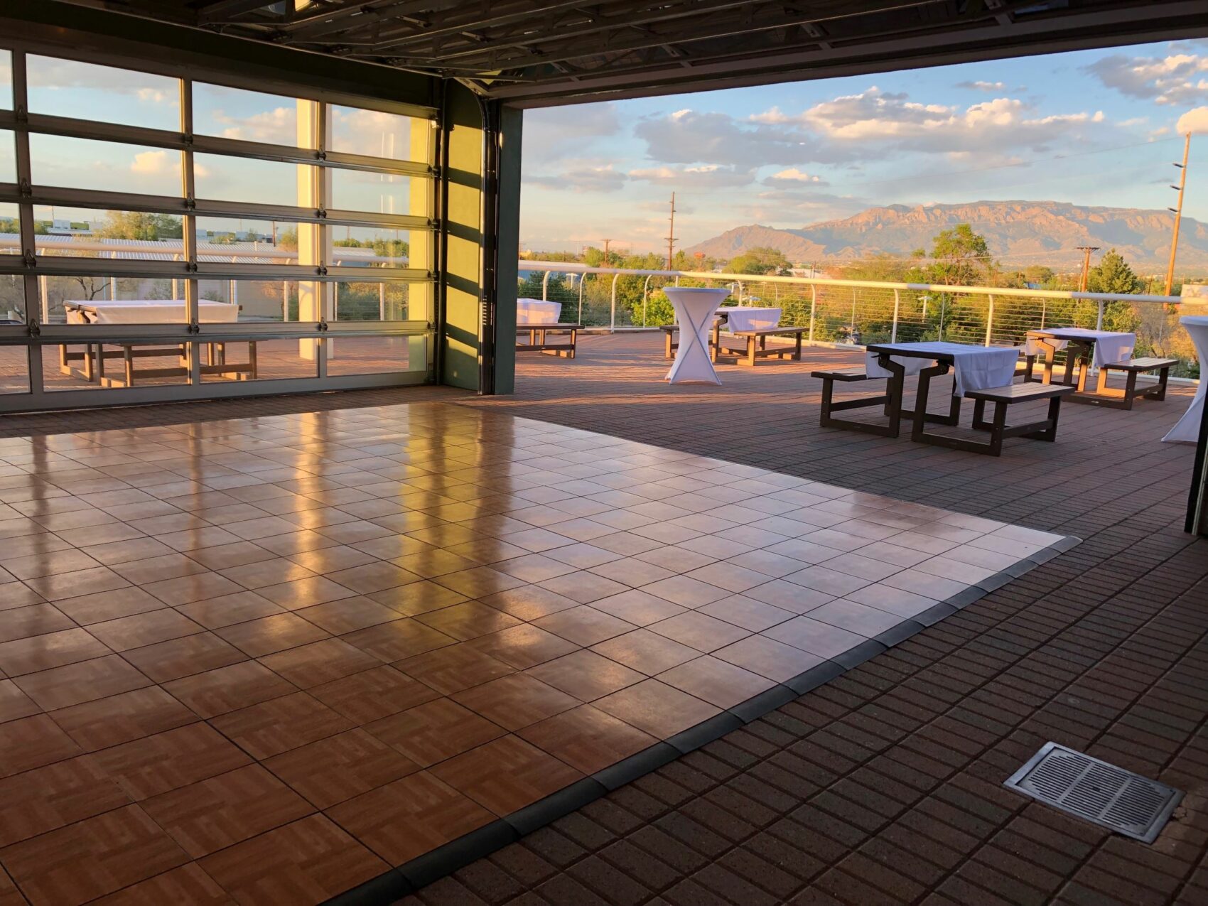 The Rotary Pavilion at Explora set up for an event, featuring a polished wooden dance floor, cocktail tables, and benches overlooking the Sandia Mountains at sunset.